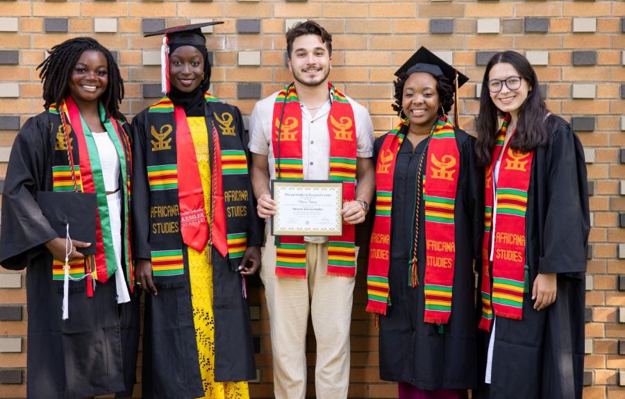 5 undergraduate students at the Africana graduation. They're smiling and holding their certificates while wearing graduation robes and colorful garbs.